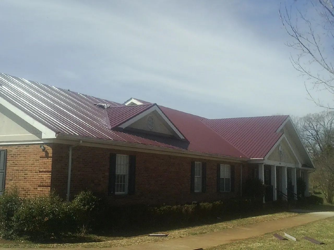 Red metal roof with gabled entries on a long brick building, from a Hail Damage Roof Repair job in Montgomery