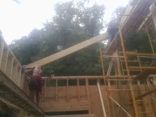 Carpenter raising a rafter beam on a new second story frame in Montgomery