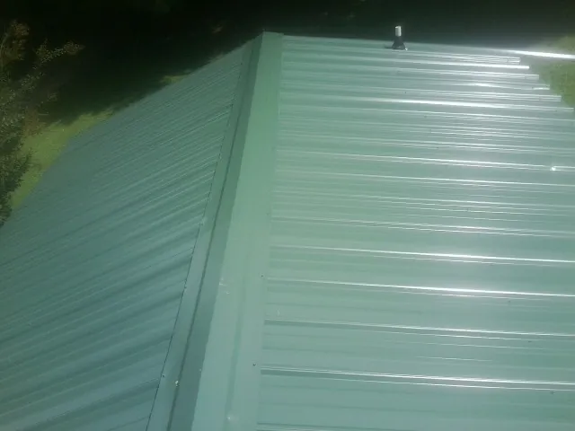 New green metal panels meeting at the ridge of a roof — Flat Roof Repair work by our crew in Montgomery