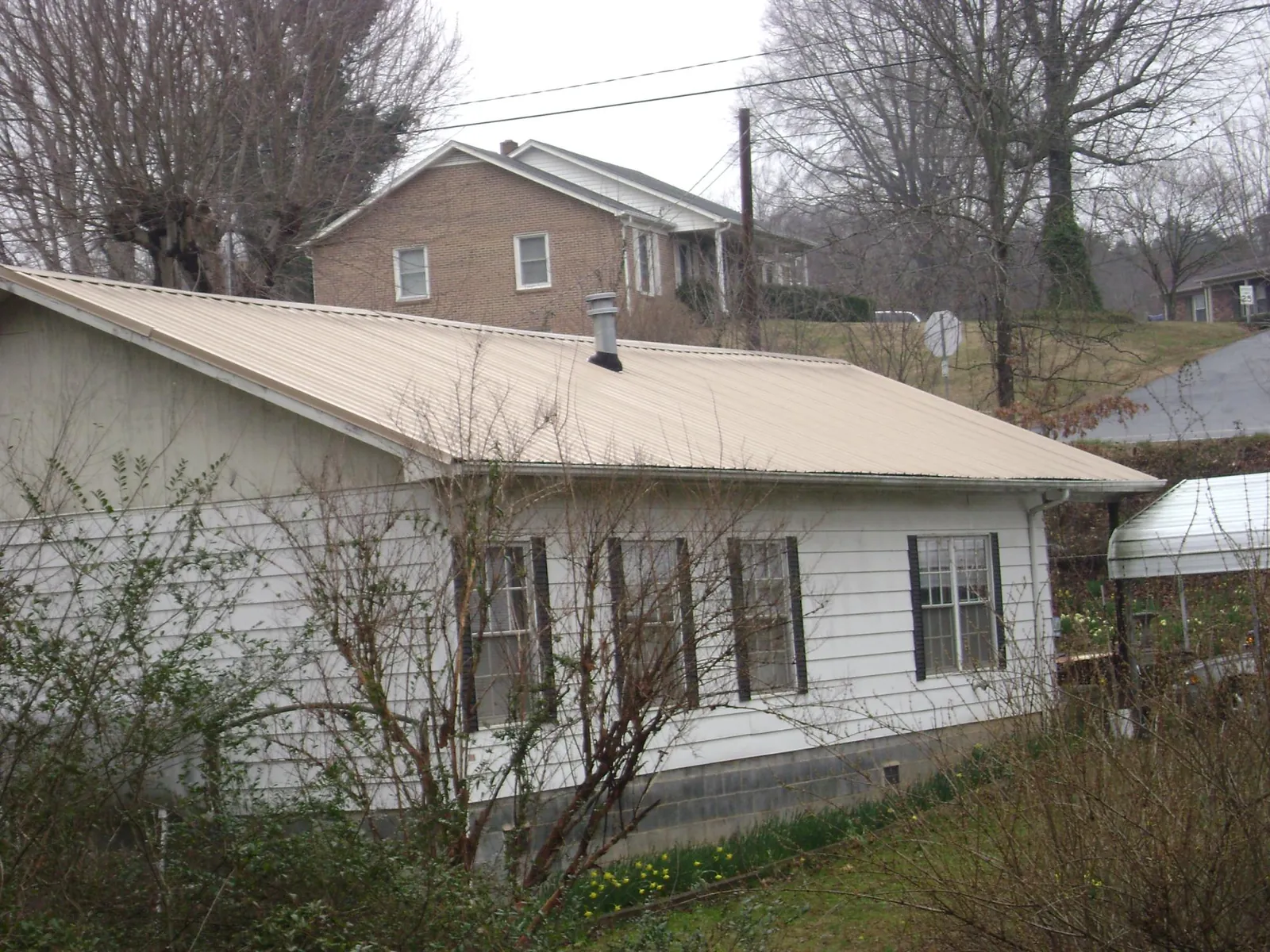 Tan metal roof on a white sided house set into a hillside — Commercial Roofing by Roofing Brothers in Montgomery